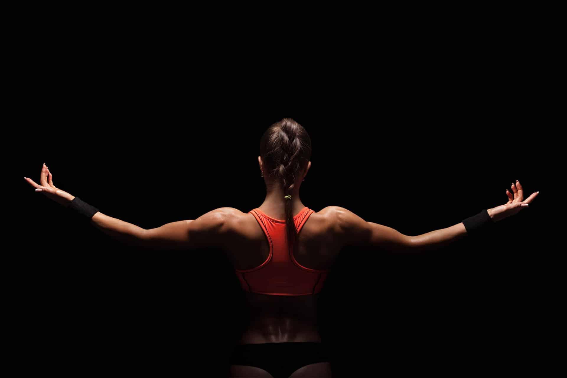 Female upper back with arms extended against black background