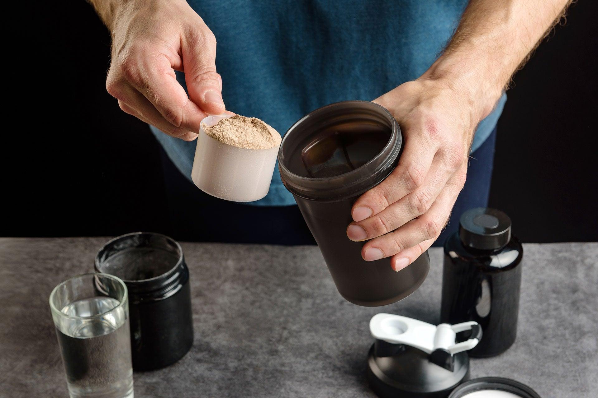Male bodybuilder scooping protein powder into shaker bottle