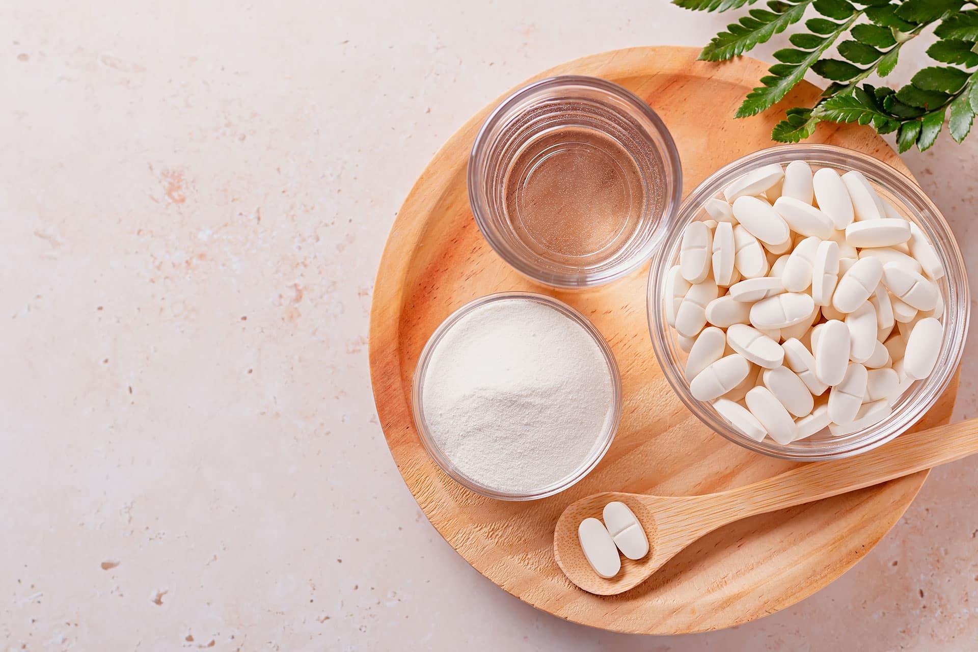 Overhead view of powder and tablet supplements in glass bowls arranged on a wooden tray