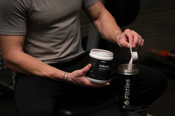 Athlete scooping FitBoost+ into a shaker at the gym