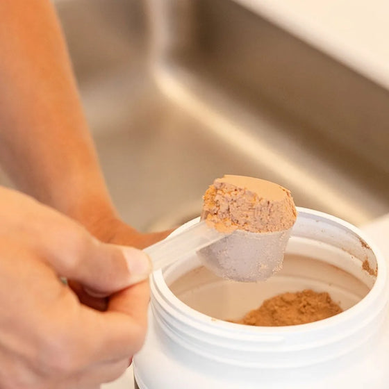 Hand scooping chocolate FitPlant+ plant protein powder from the tub