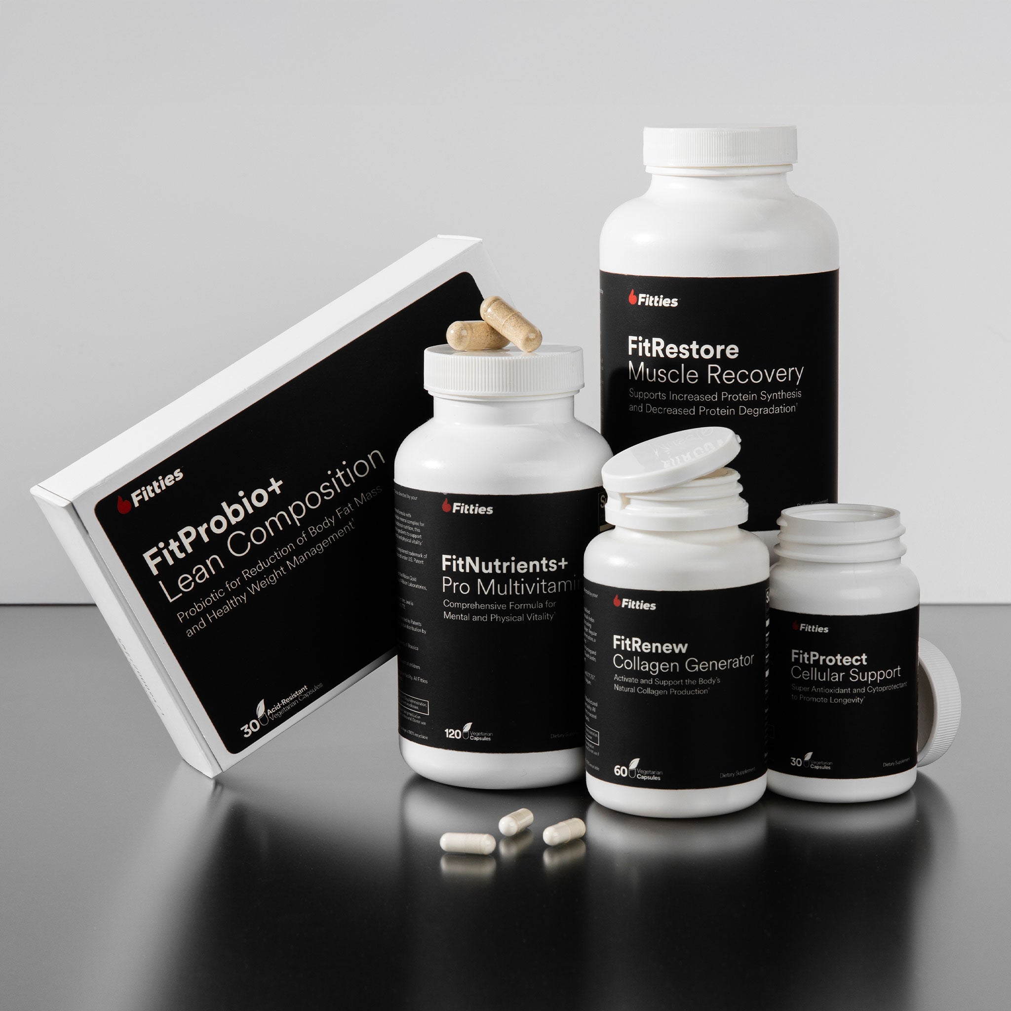 Collection of Fitties supplement bottles and packaging on a reflective surface with a gray background