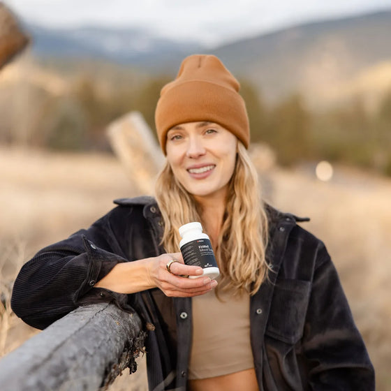 Woman outdoors holding a bottle of Fitties FitWell