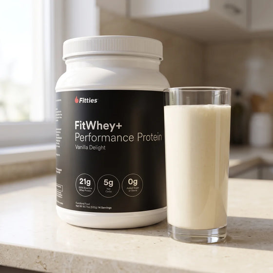 FitWhey+ Vanilla grass-fed whey protein tub on a kitchen counter beside a glass of vanilla protein shake