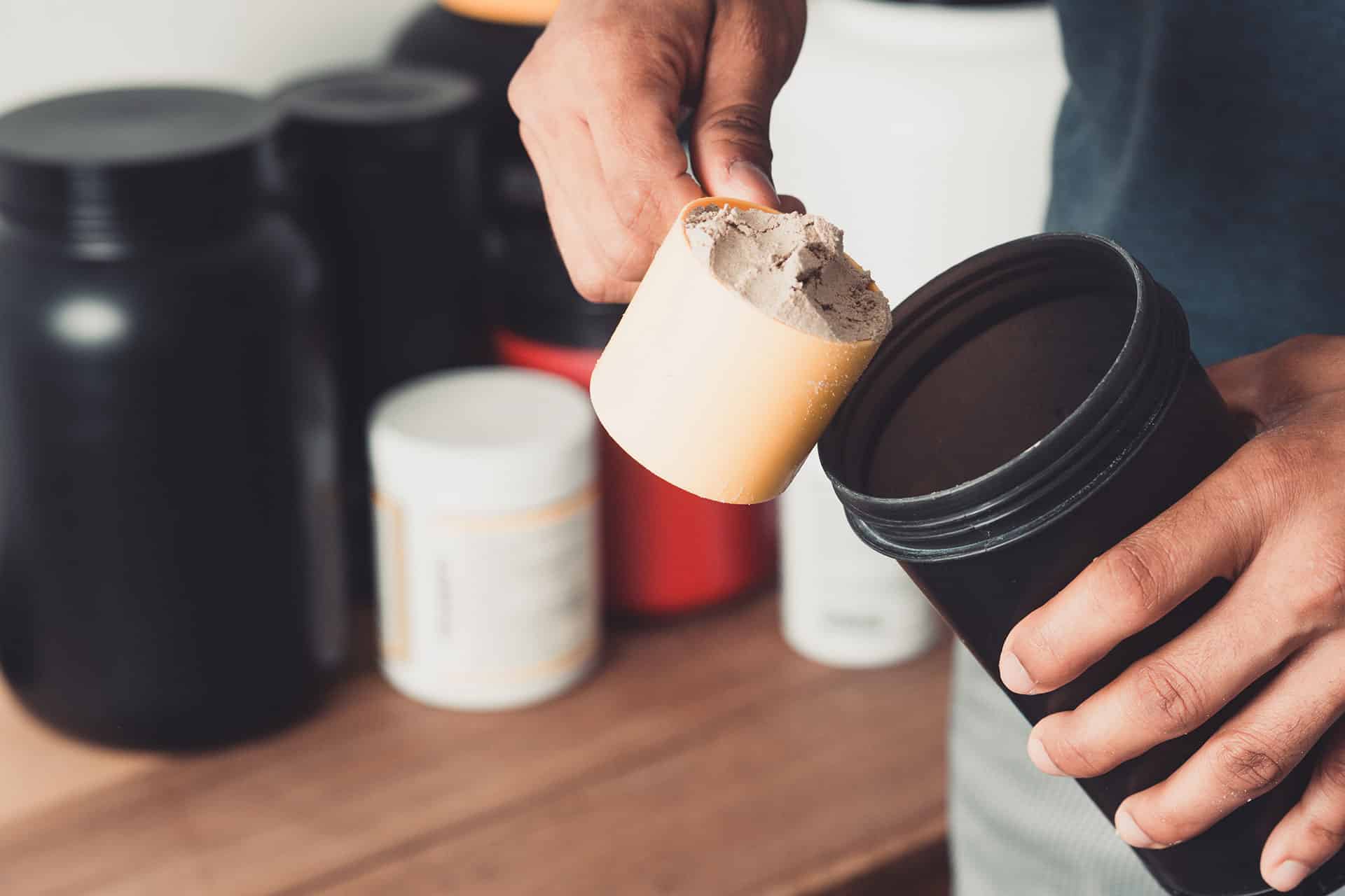 Closeup of a man scooping vanilla protein powder into a black shaker bottle