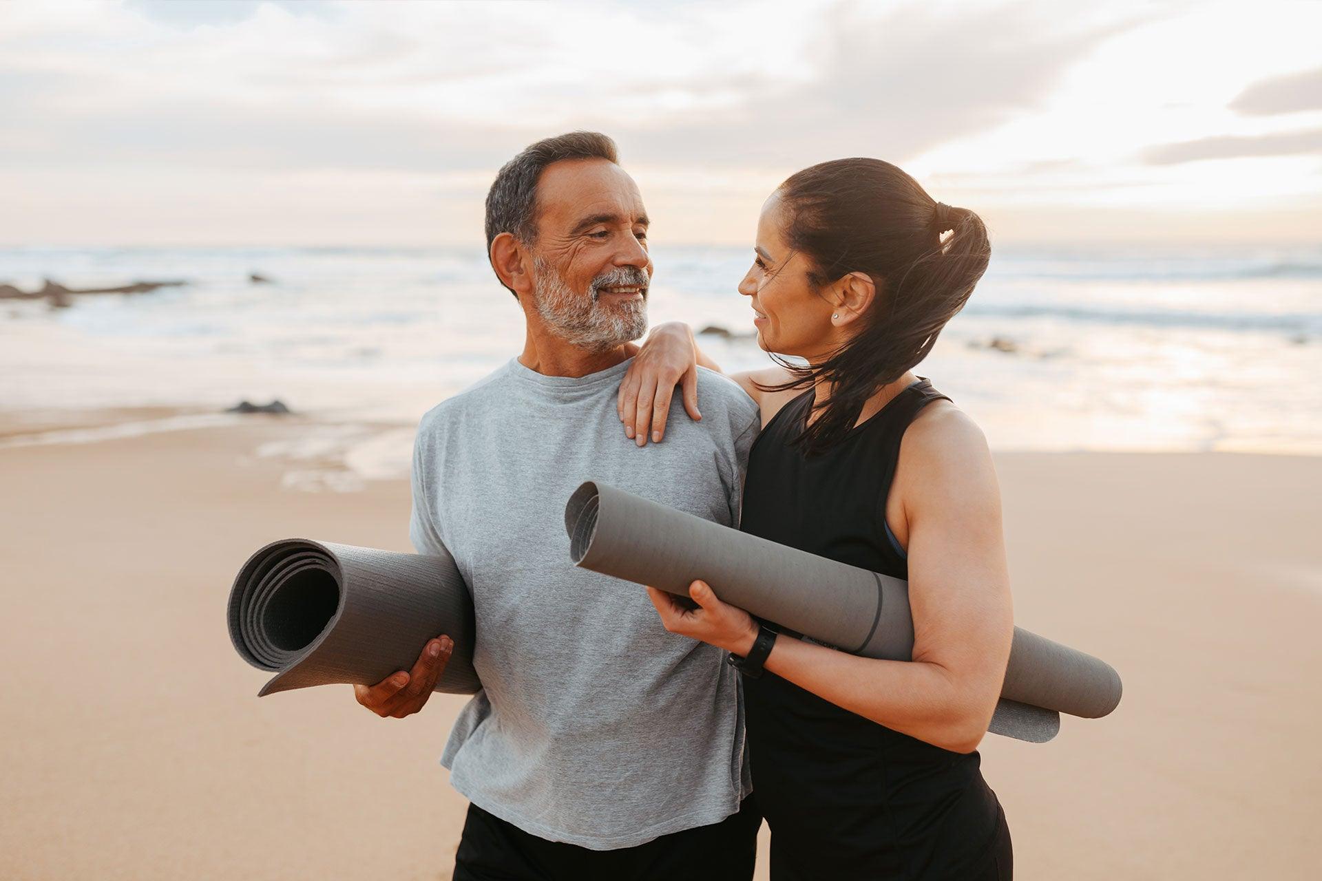 Male and female with yoga mats on beach