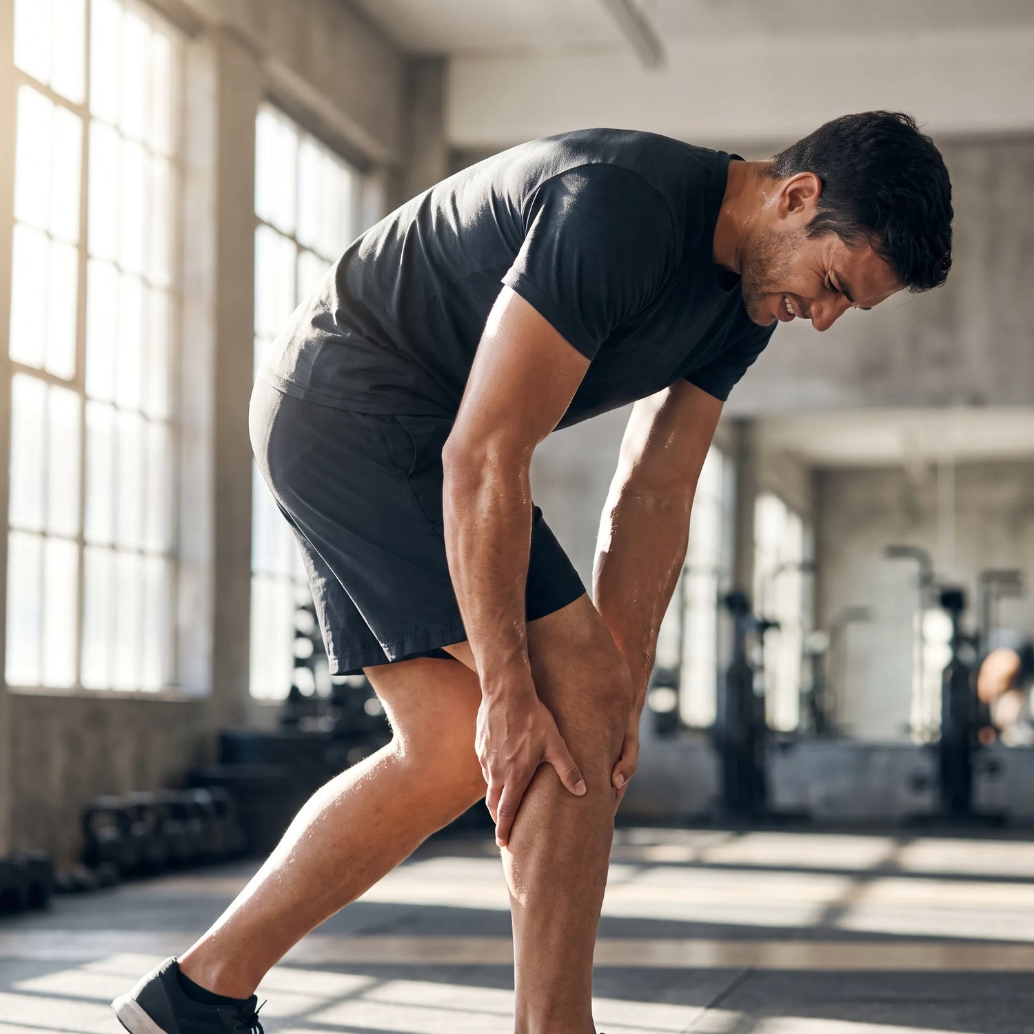 Athlete in a gym gripping a cramping leg muscle during a workout