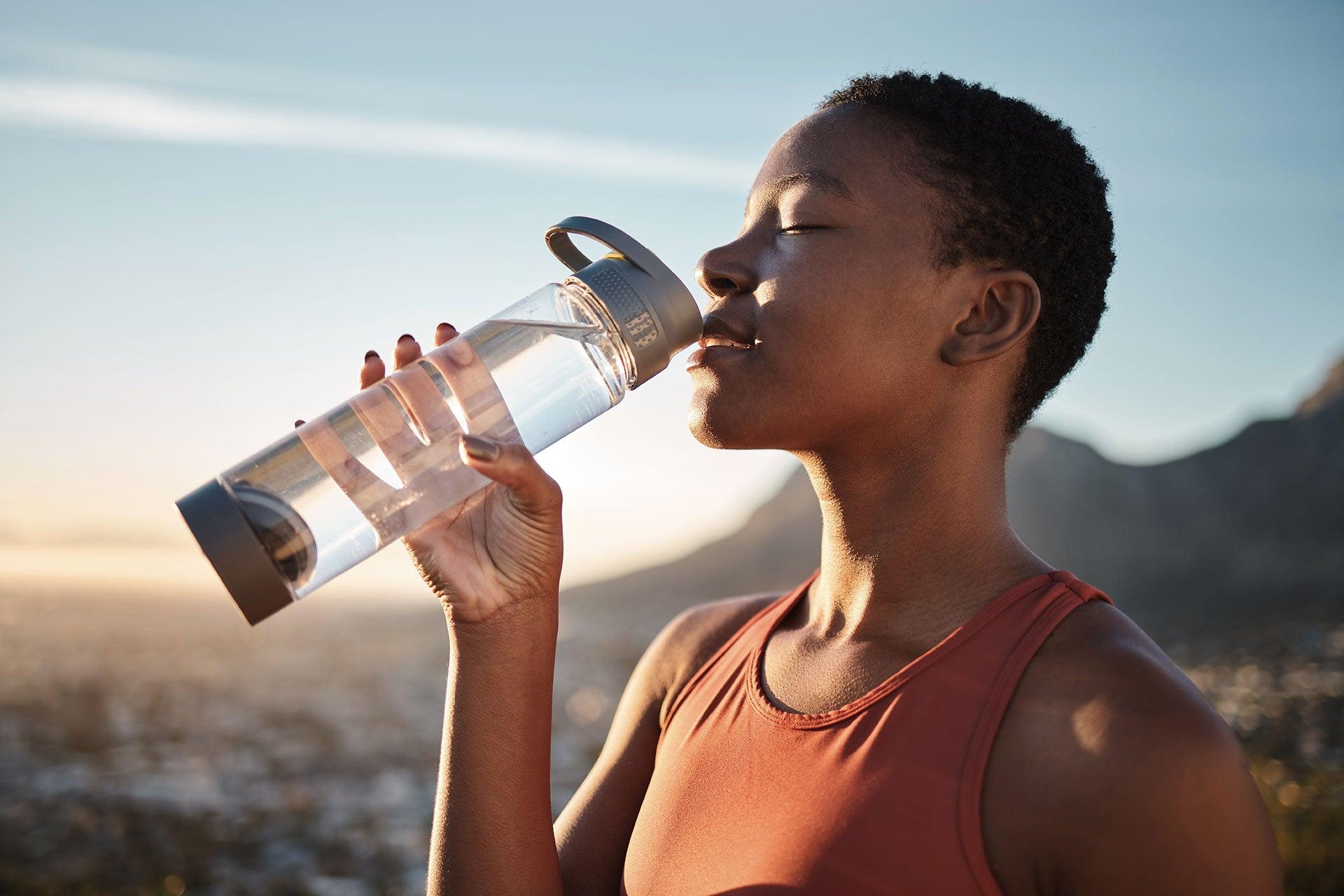 Fit female breaking to drink from water bottle during outdoor workout