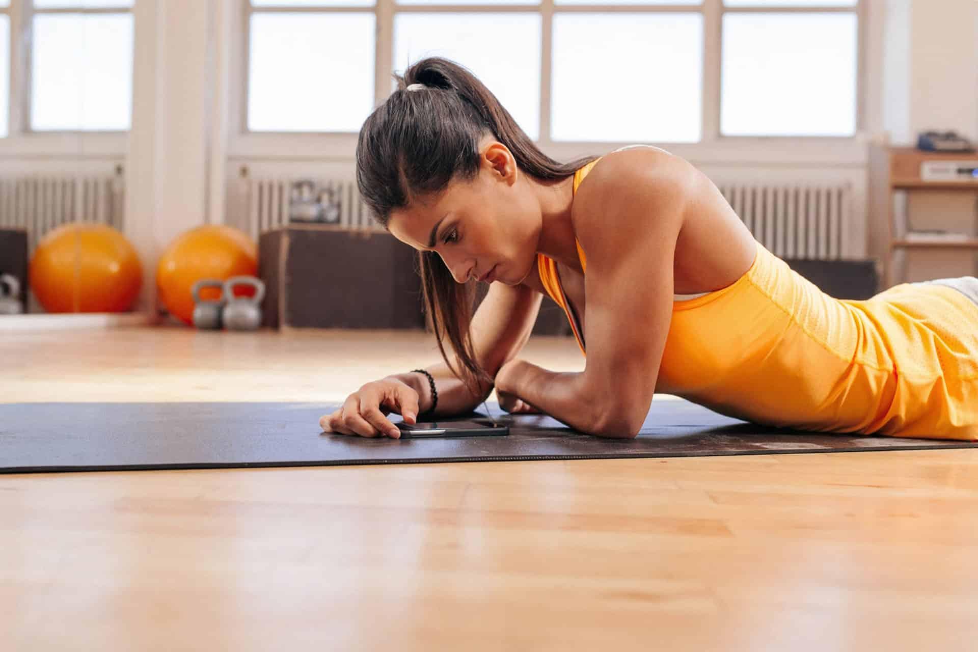 Female lying on cardio room floor with smartphone