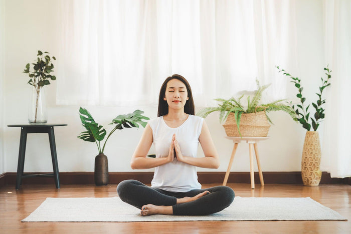 Woman meditating cross-legged at home in a calm, sunlit room