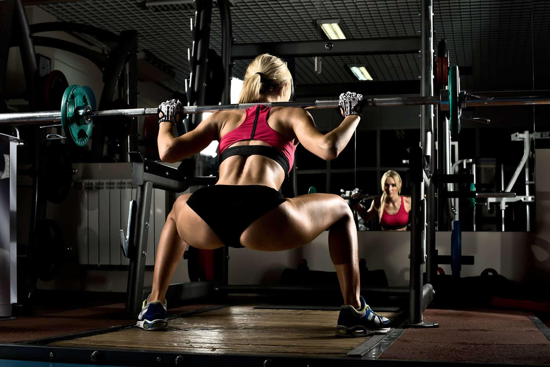Female performing sumo squats with barbell and squat rack