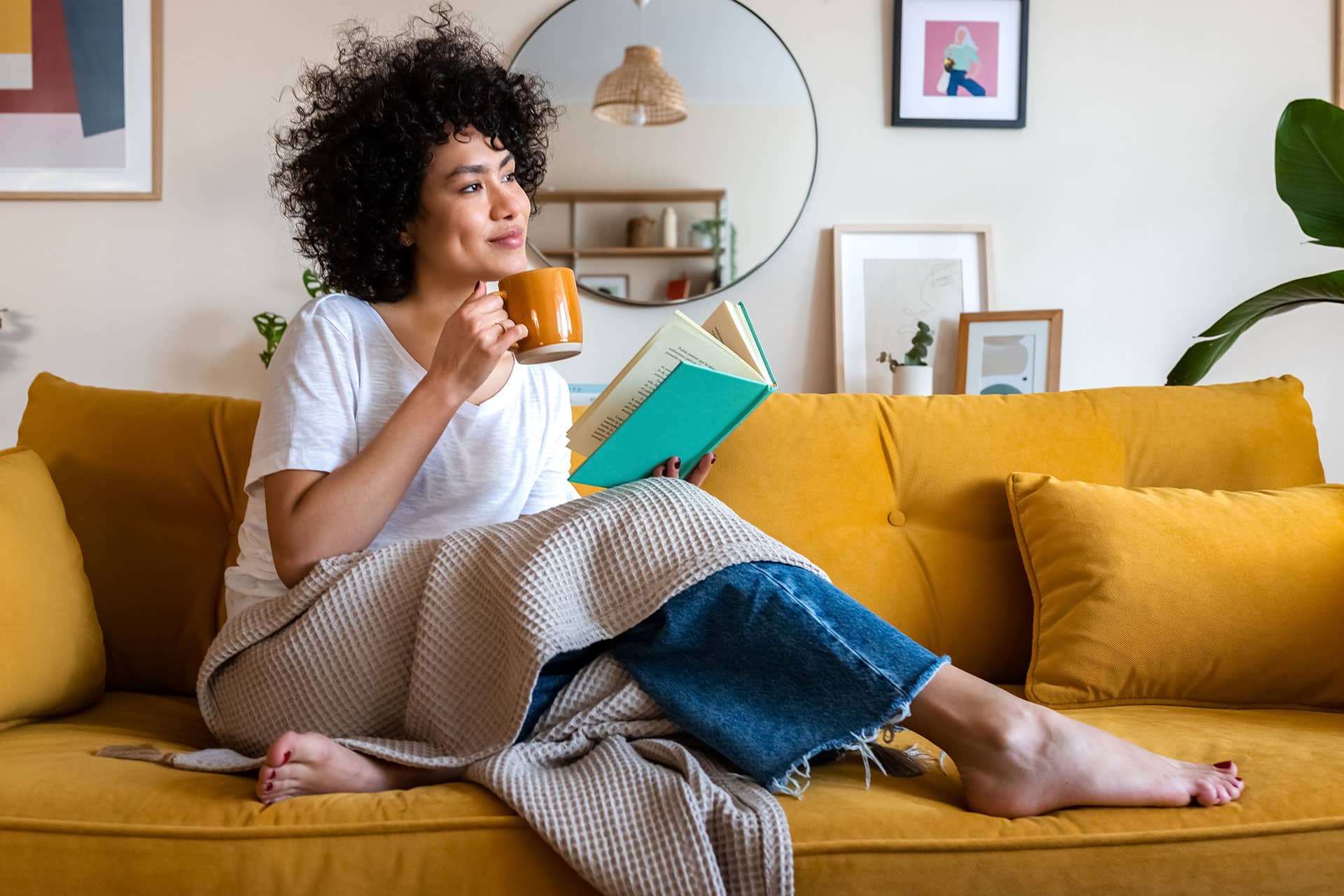 Woman relaxing on a sofa with a coffee while reading a book