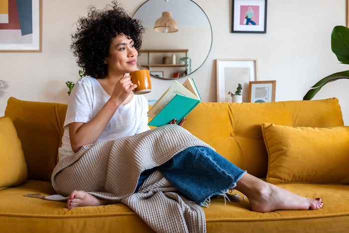 Woman relaxing on a sofa with a coffee while reading a book