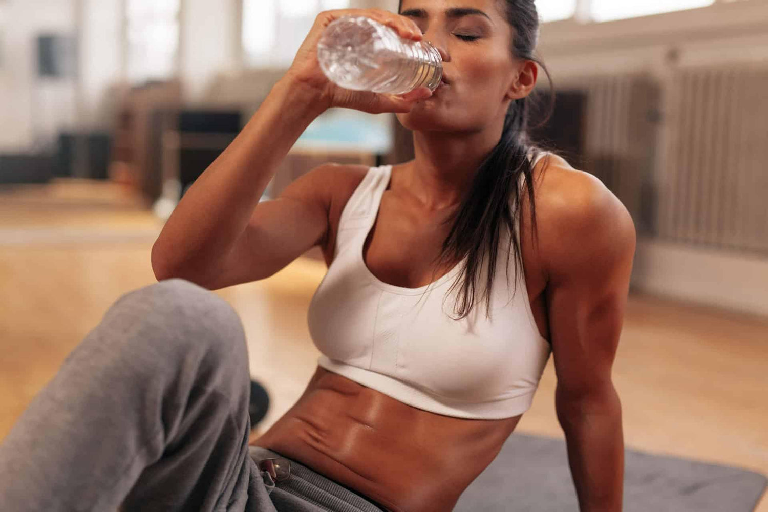Female sitting on floor drinking BCAAs from water bottle