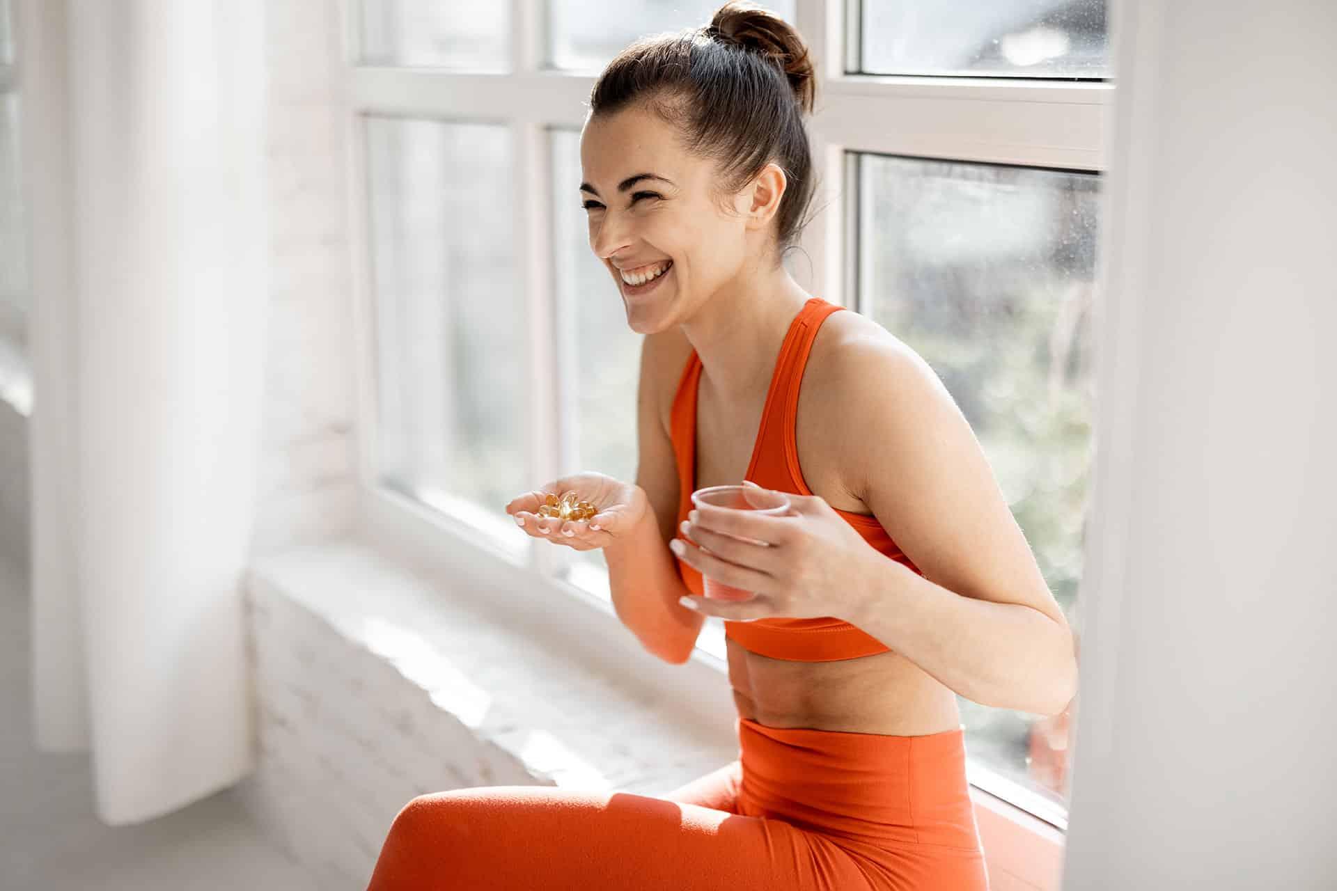 Fit female smiling while taking handful of supplement pills