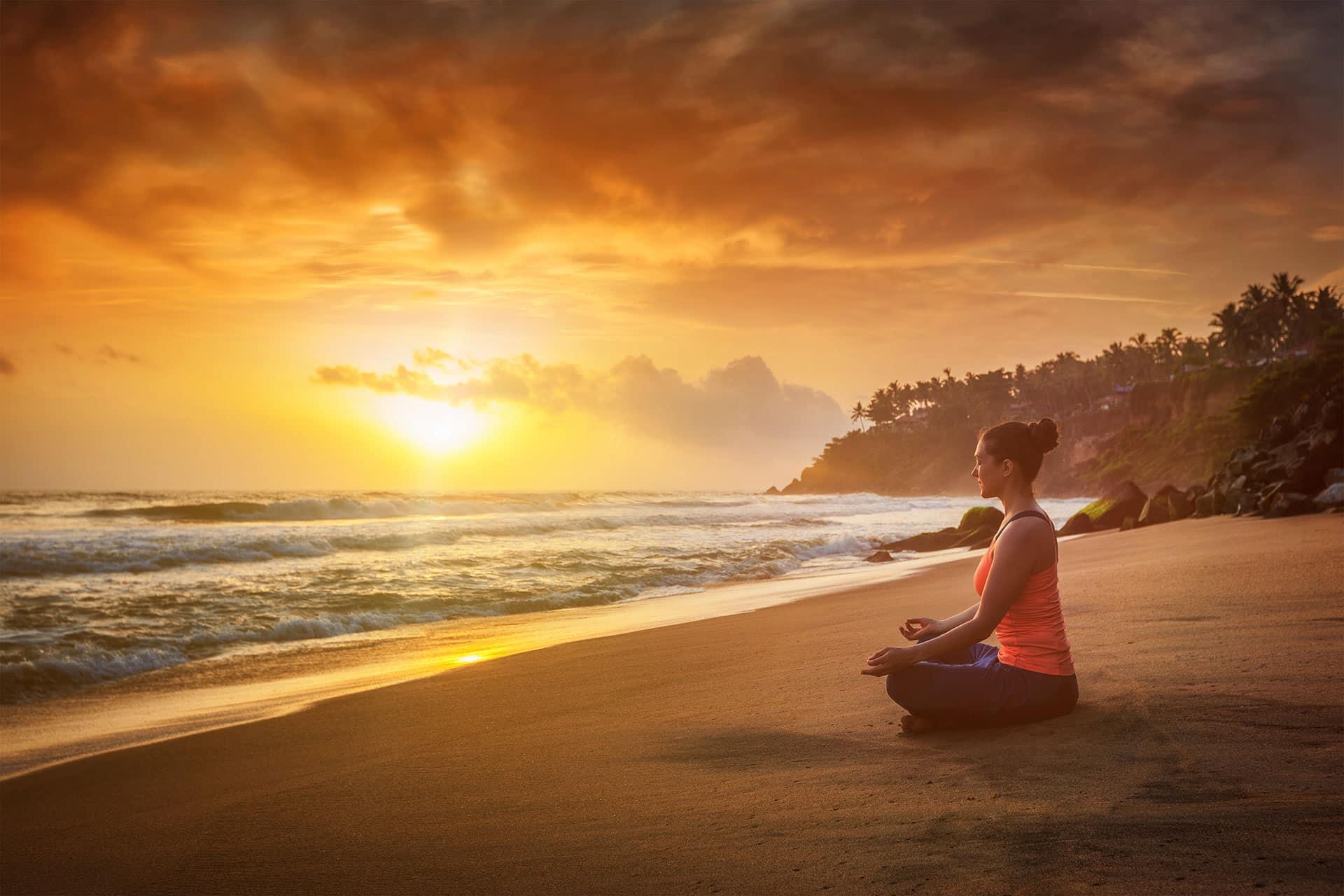 Fit woman doing yoga meditation on a beach during sunset