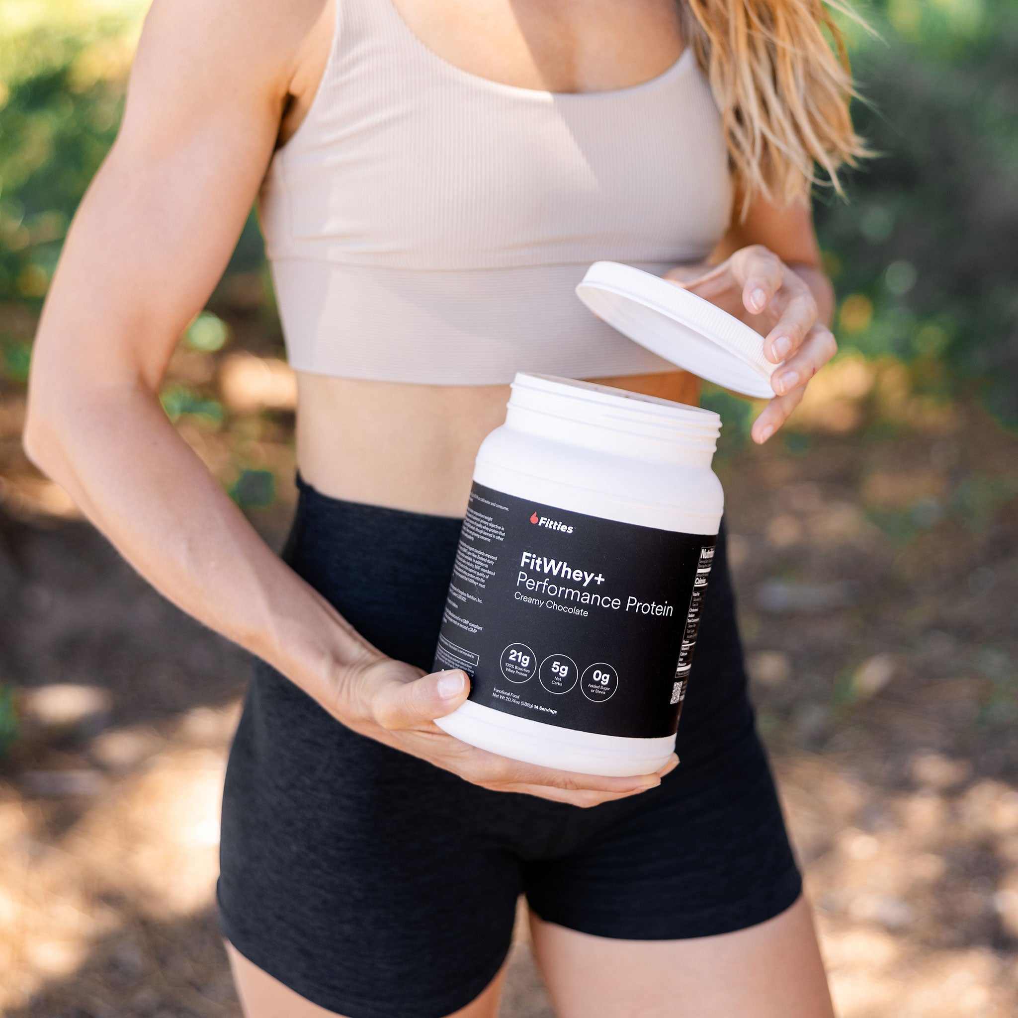 Woman in athletic wear outdoors opening a tub of Fitties FitWhey+ Performance Protein
