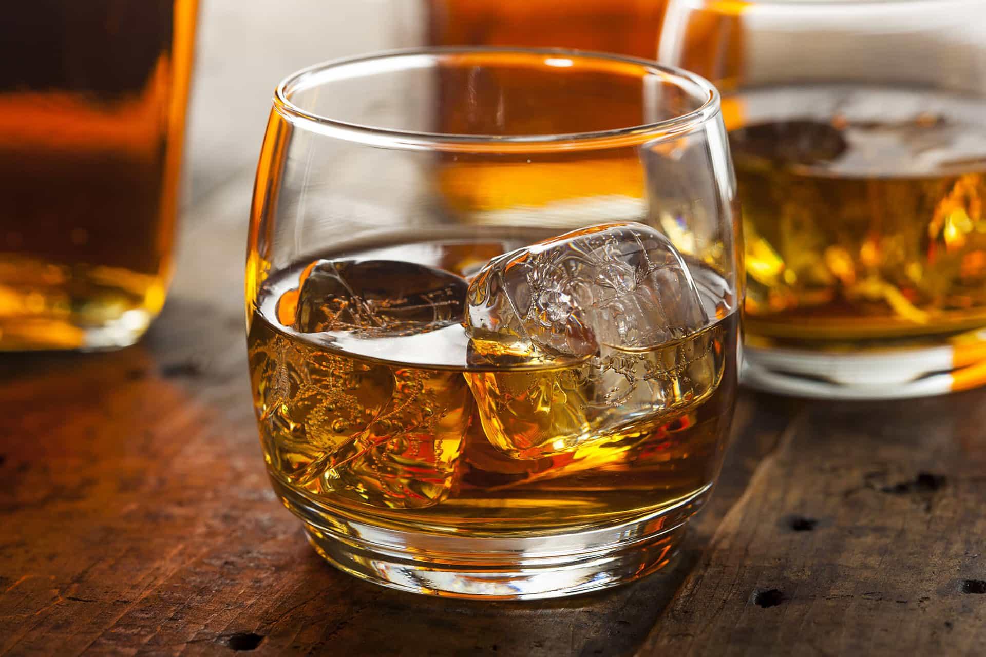 Closeup of whiskey in rocks glasses with ice on dark surface