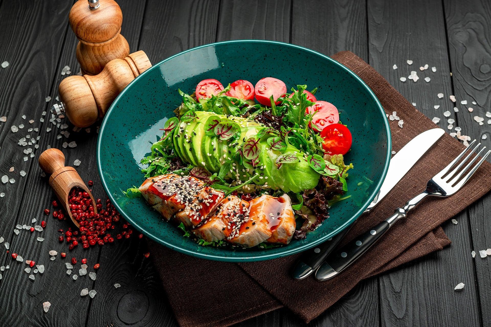 Closeup of keto-friendly salad in teal bowl on black wood tabletop