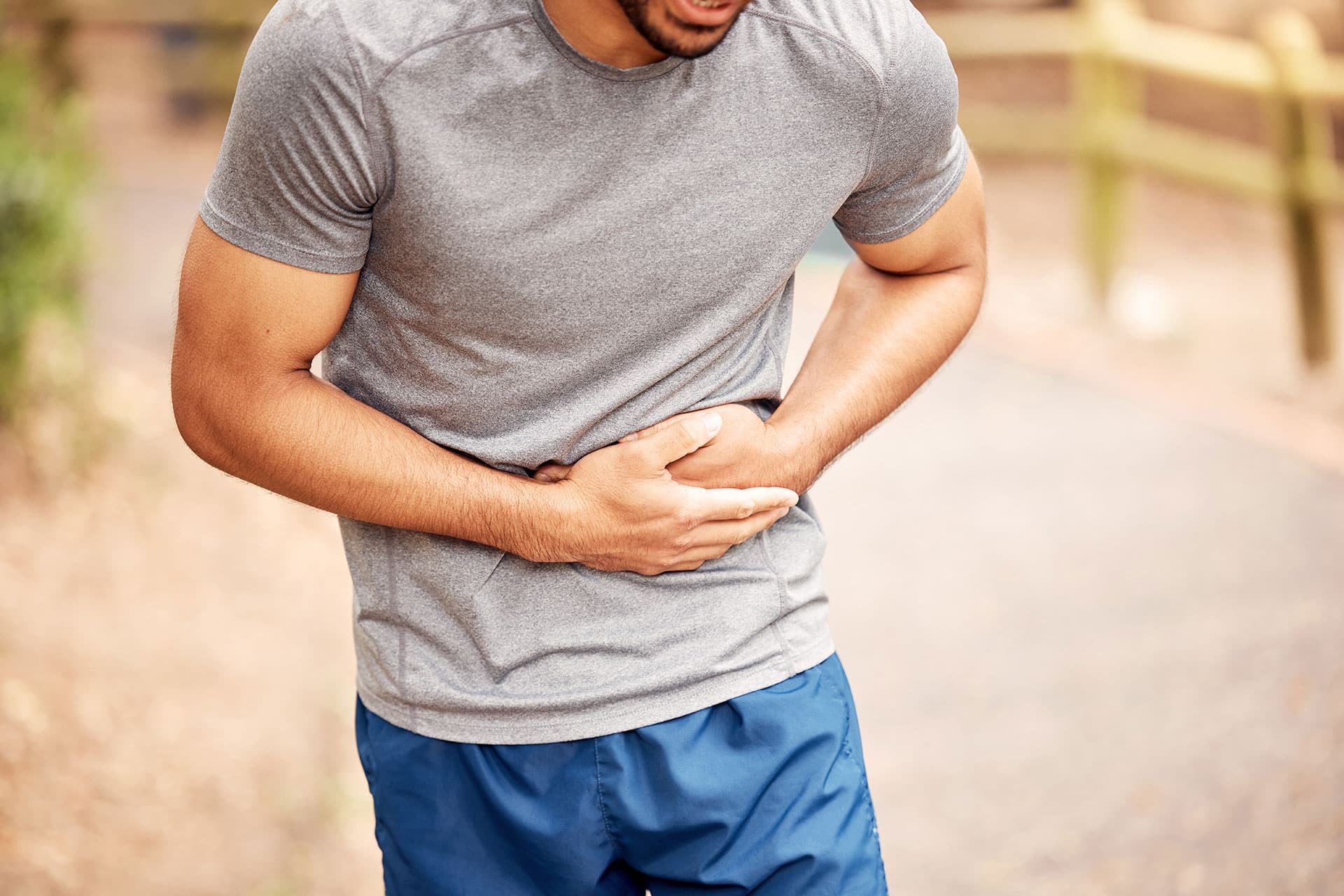Athlete holding his stomach during outdoor exercise, experiencing digestive discomfort