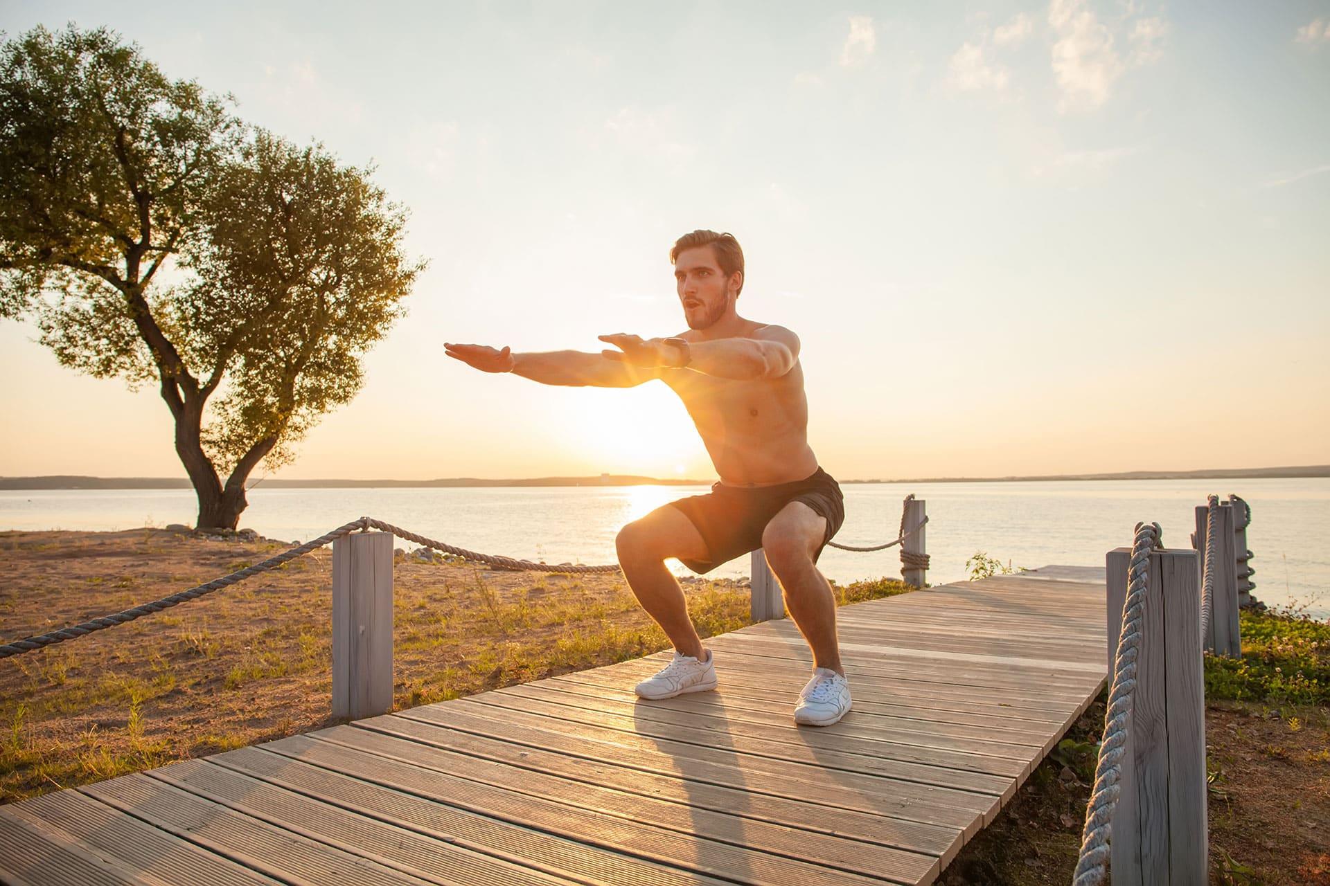 Male athlete performing a bodyweight squat on an outdoor dock during an active recovery session