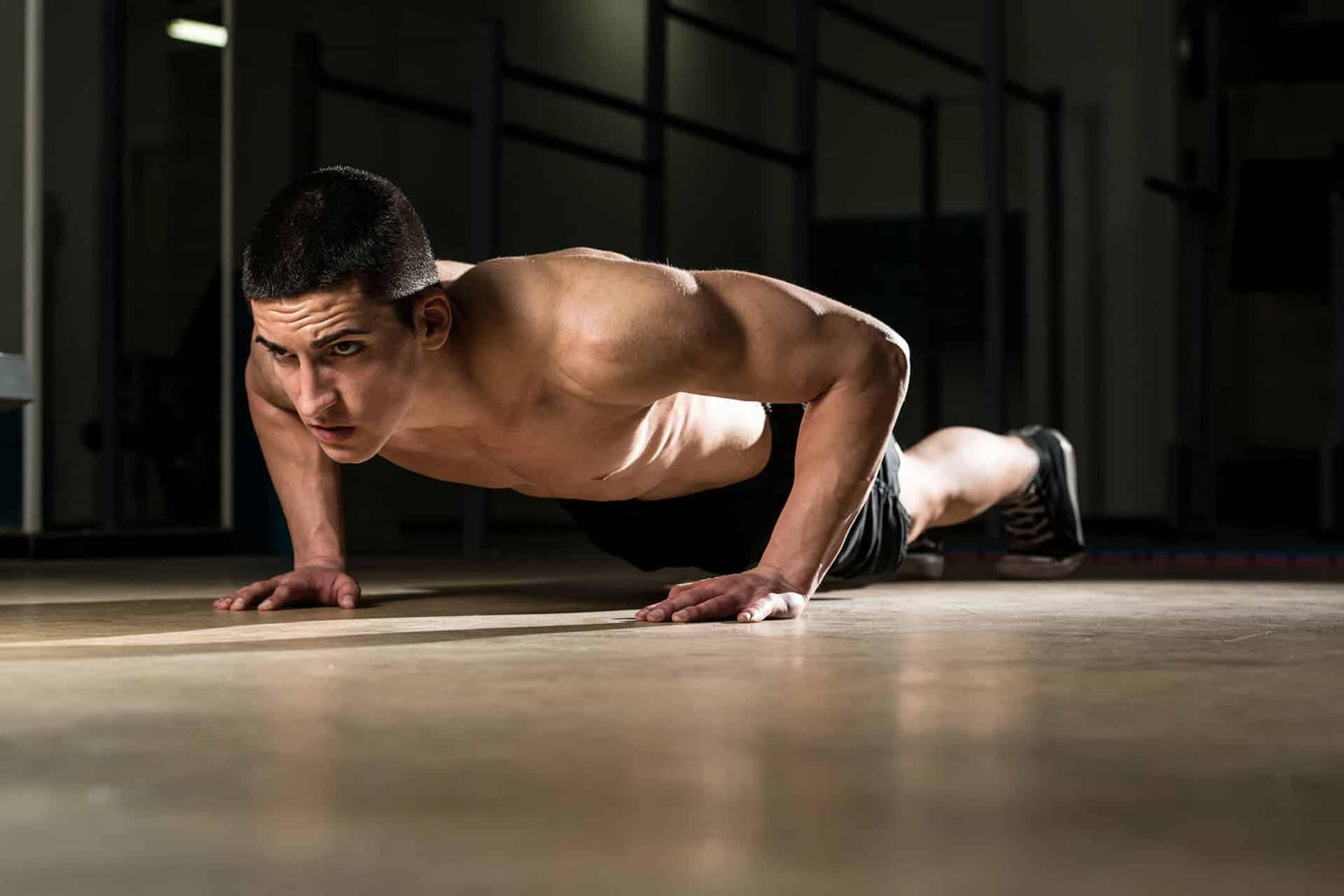 Fit male performing pushups in dimly lit gym