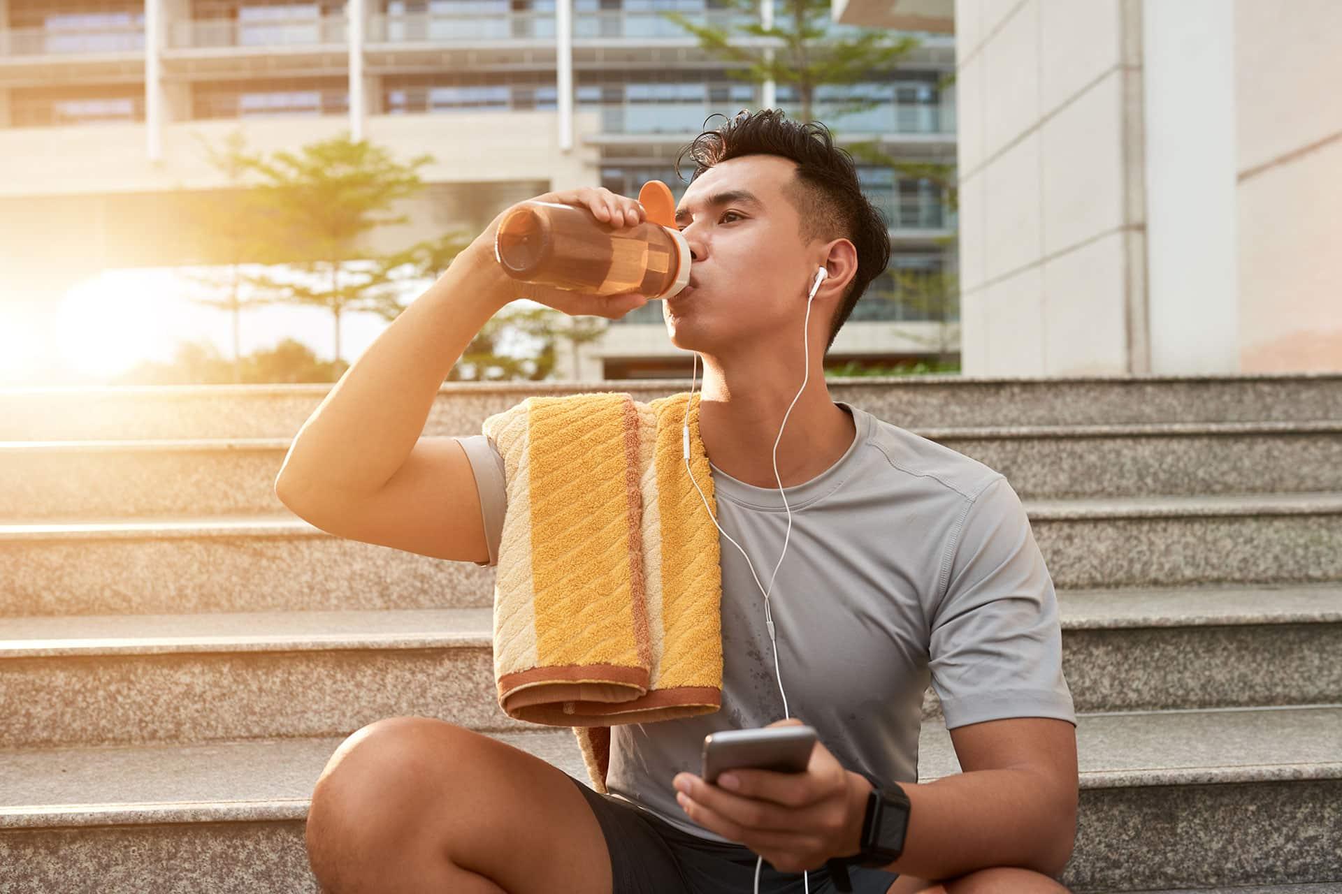 Fit male breaking to drink from water bottle during outdoor workout