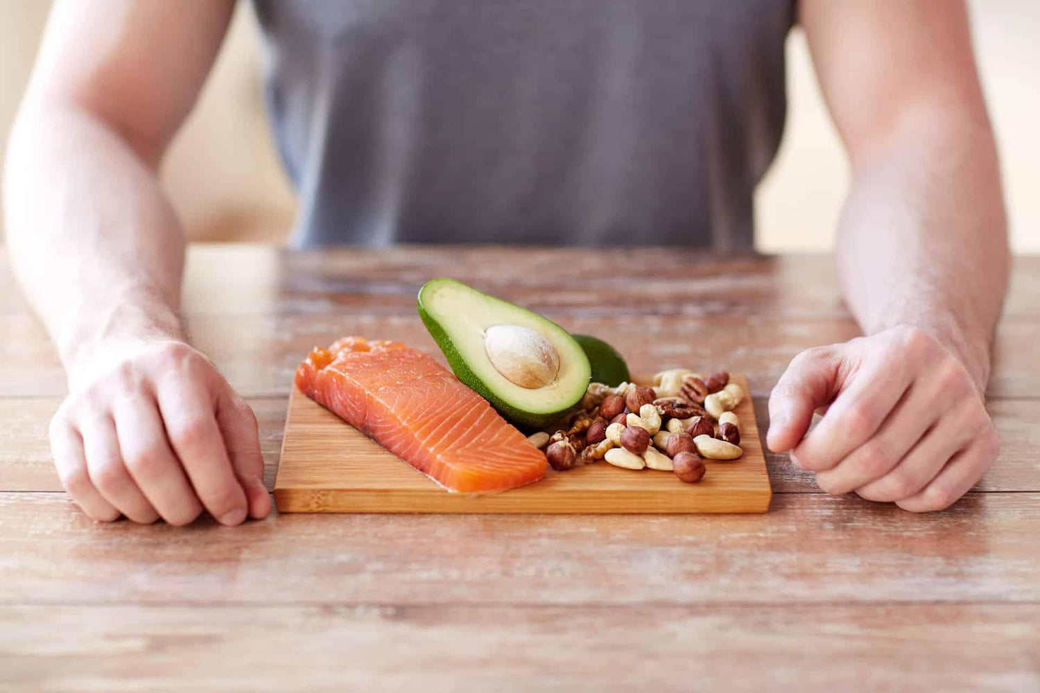 Closeup of male sitting at table with salmon, avocado, and mixed nuts on wood tray