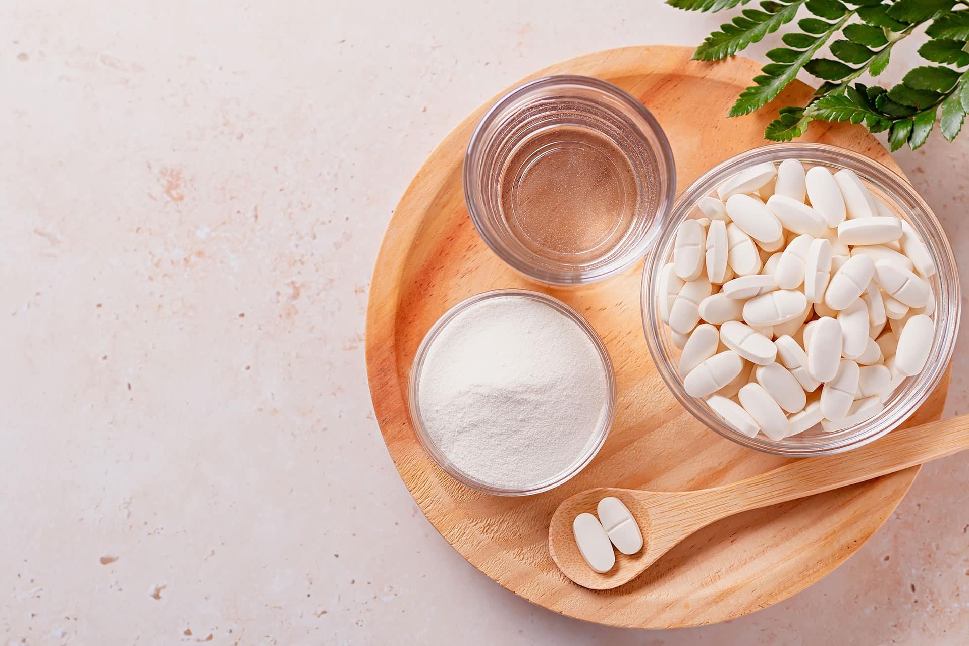 Overhead view of powder and tablet supplements in glass bowls on wood tray