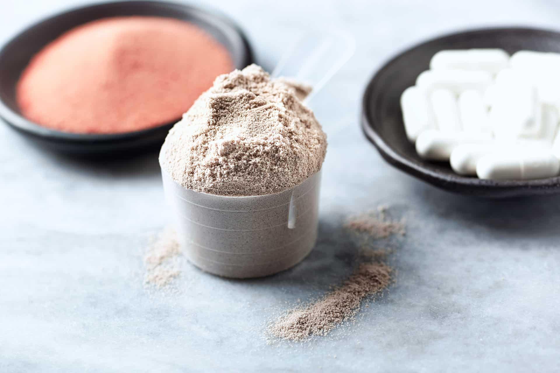 Closeup of scoop of chocolate protein powder with supplements in background