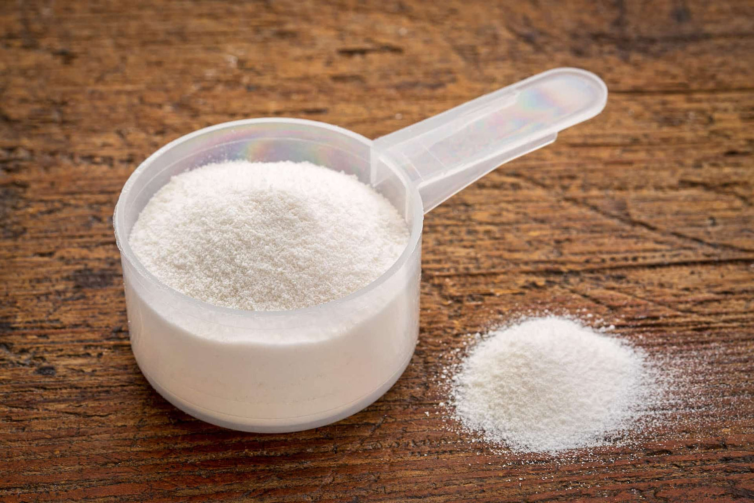 Closeup of a scoop of white supplement powder on a wooden tabletop