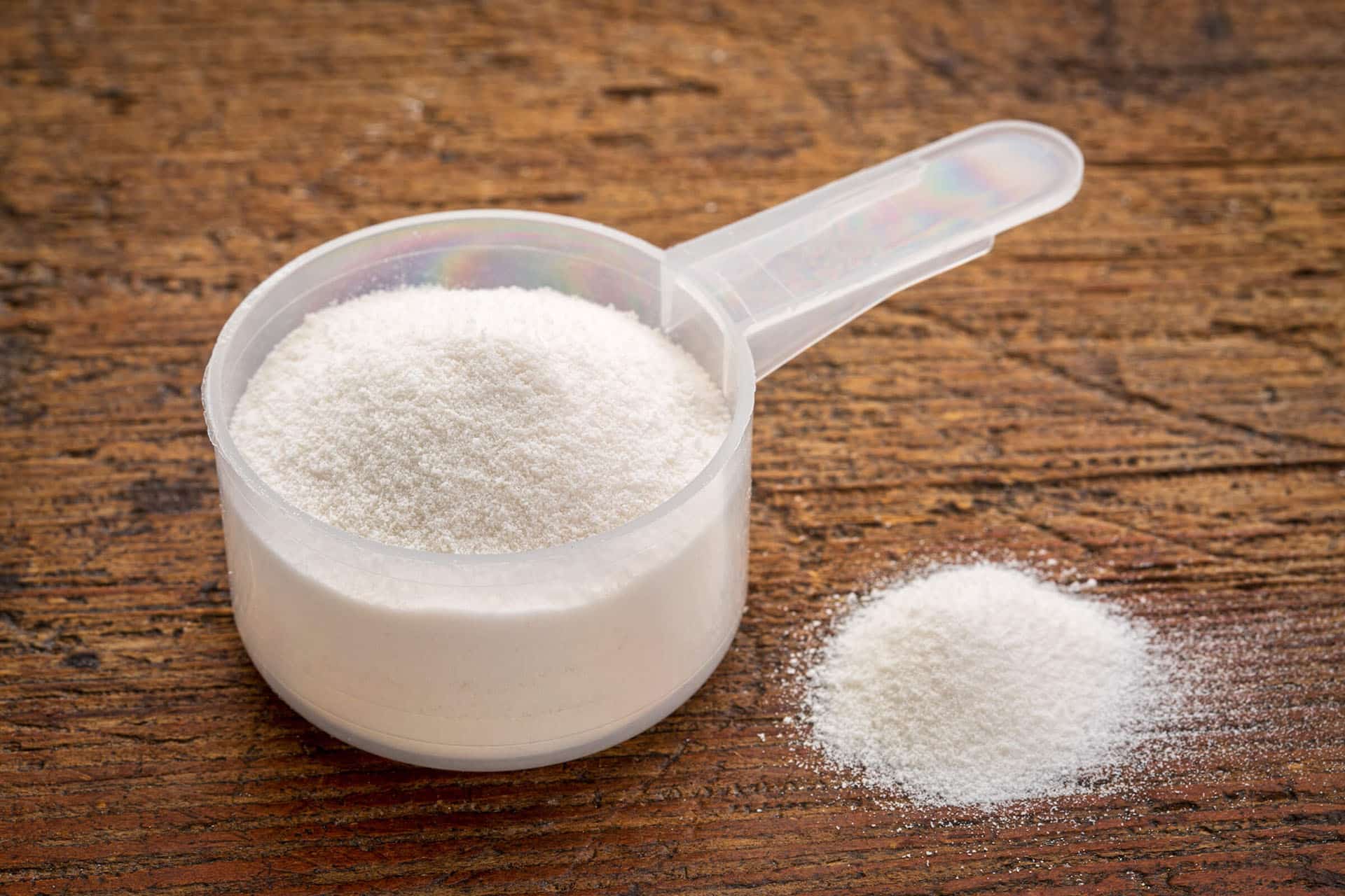 Closeup of a scoop of white supplement powder on a wooden tabletop