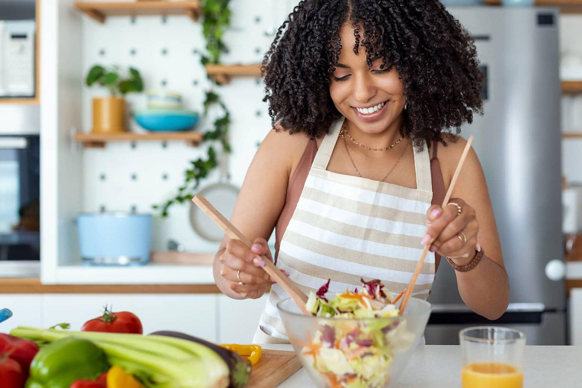 Closeup of smiling beautiful young woman preparing tasty vegan salad in the kitchen at home