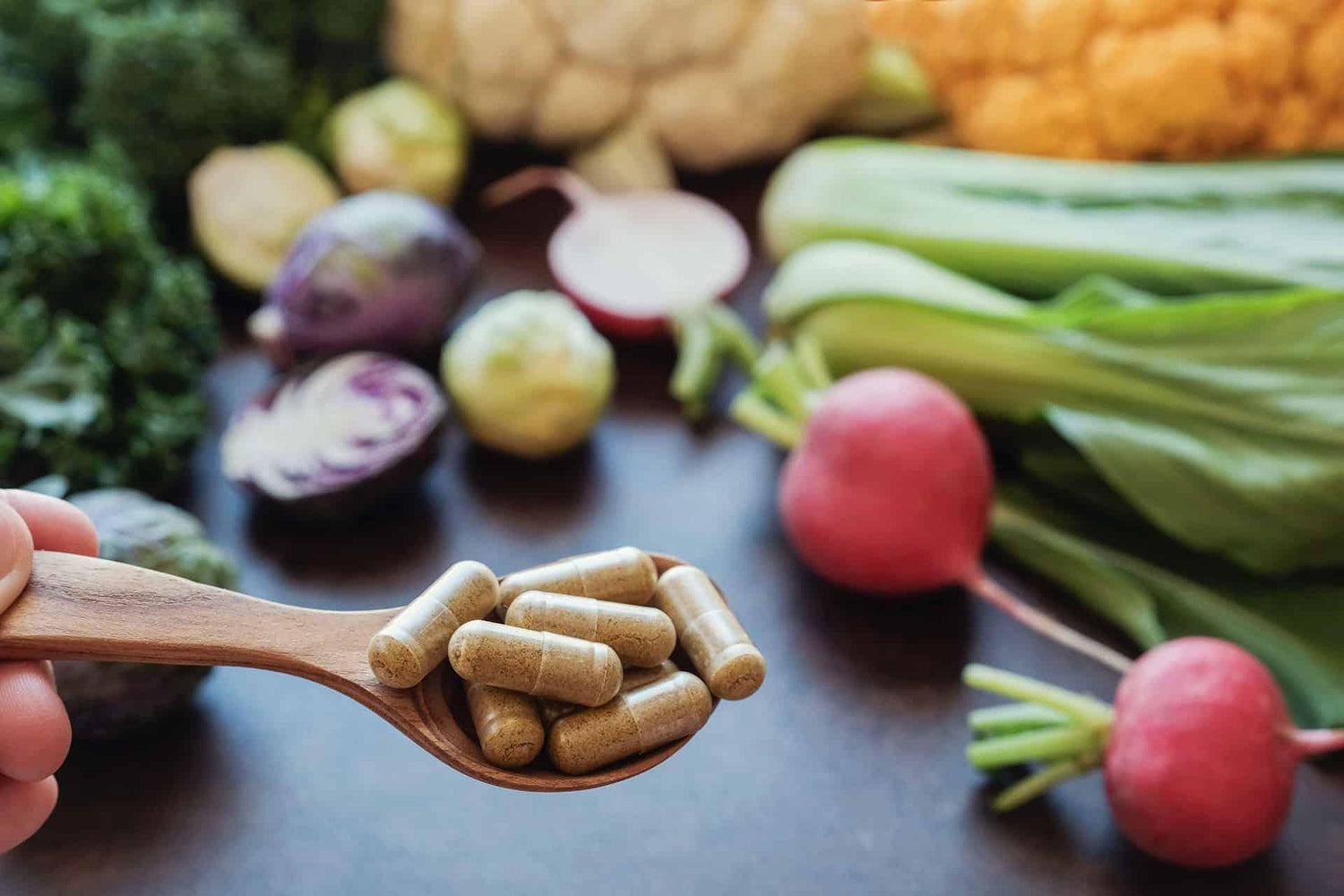 Closeup of herbal tablet supplements in wooden spoon with healthy veggies in the background