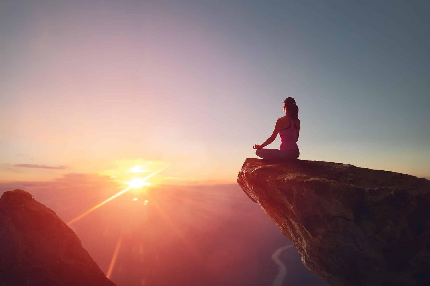 Wide angle view of woman practicing yoga meditation on a cliff with sunset