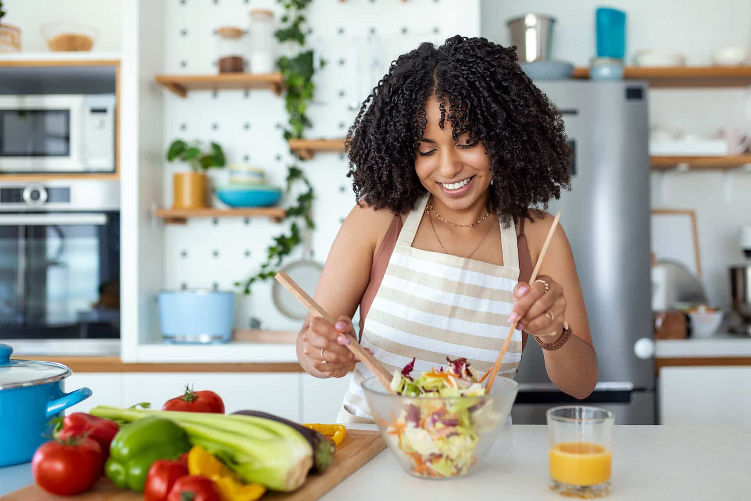 Fit female smiling while mixing salad in kitchen