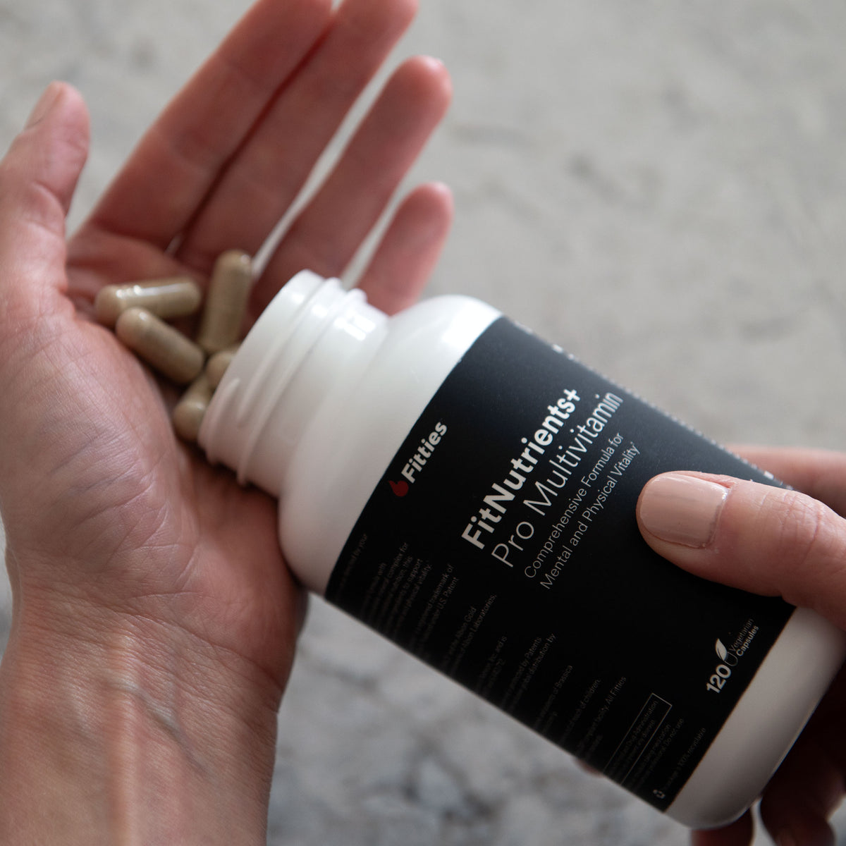 Close-up of a hand pouring Fitties FitNutrients+ capsules from the bottle into an open palm