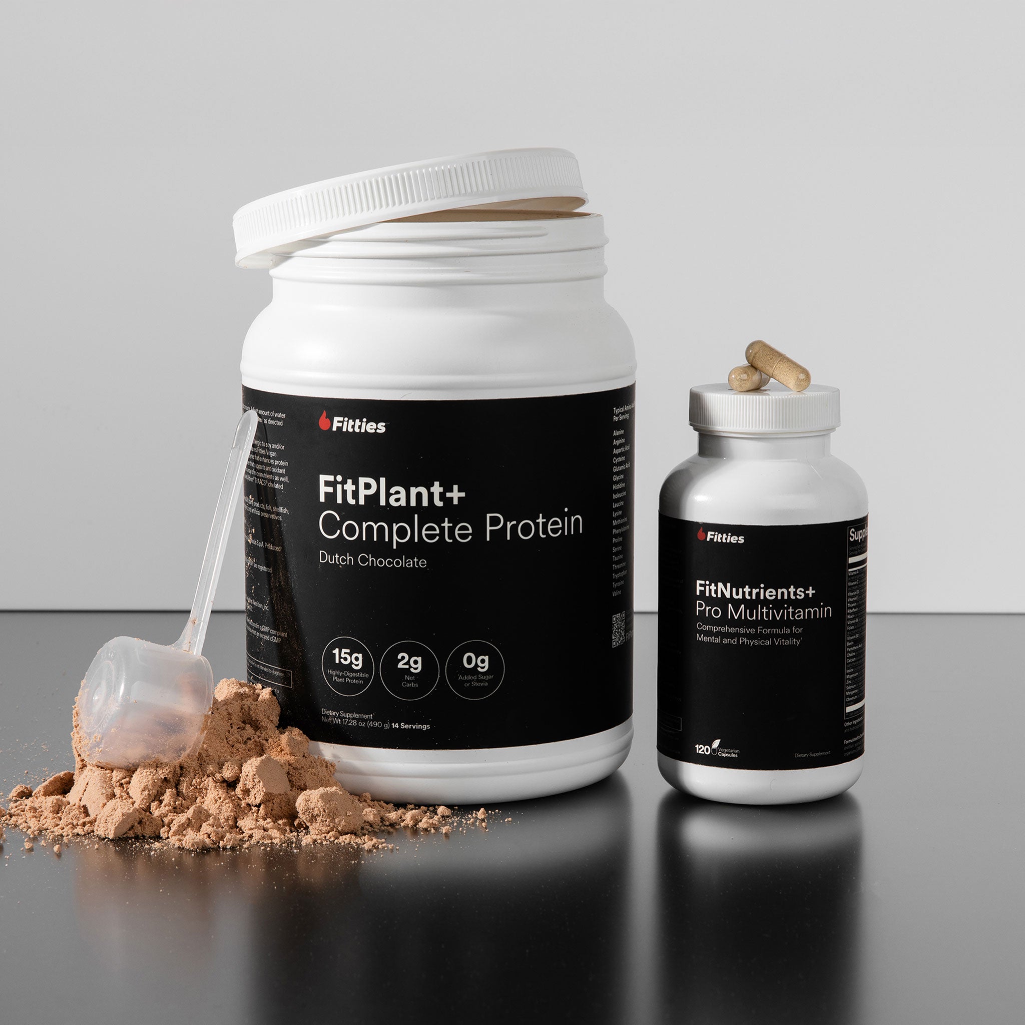 FitPlant+ Complete Protein container with scoop and FitNutrients+ Pro Multivitamin bottle on a reflective surface.