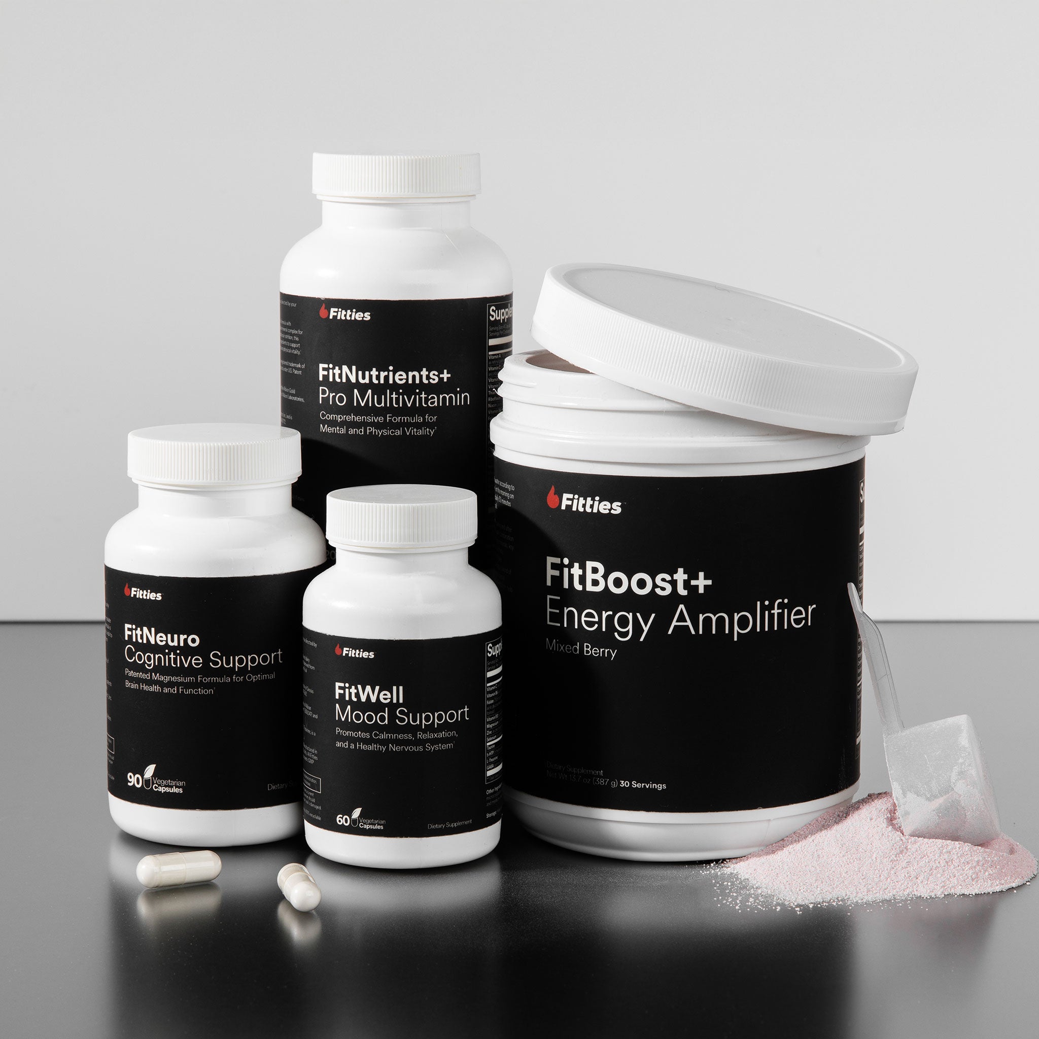 Collection of Fitties supplement products including FitNeuro, FitNutrients+, FitBoost+, and FitWell on a gray surface.