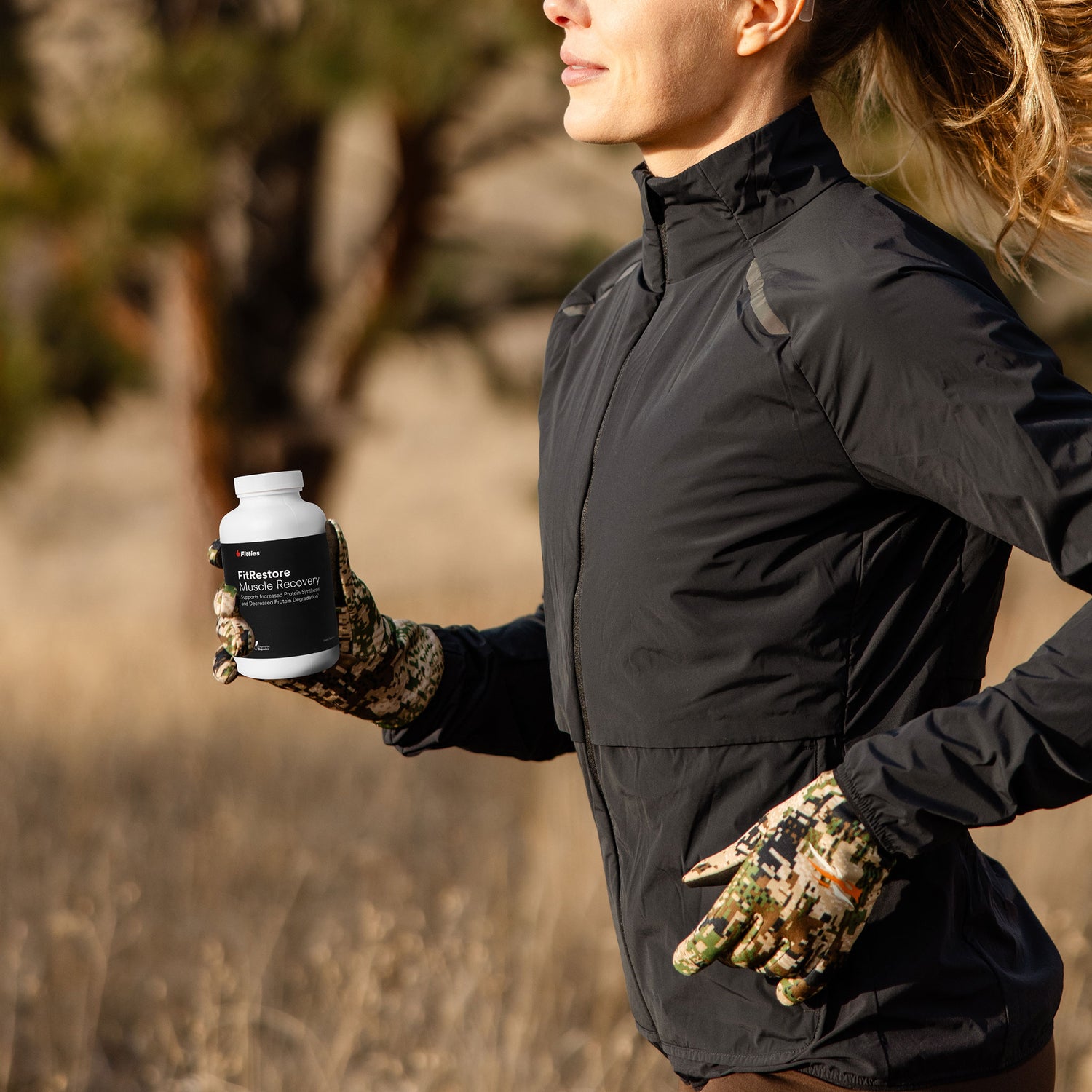 Female athlete running in nature with a bottle of Fitties FitRestore