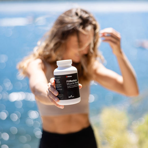 Fitness model holding bottle of Fitties FitRestore with lake in background