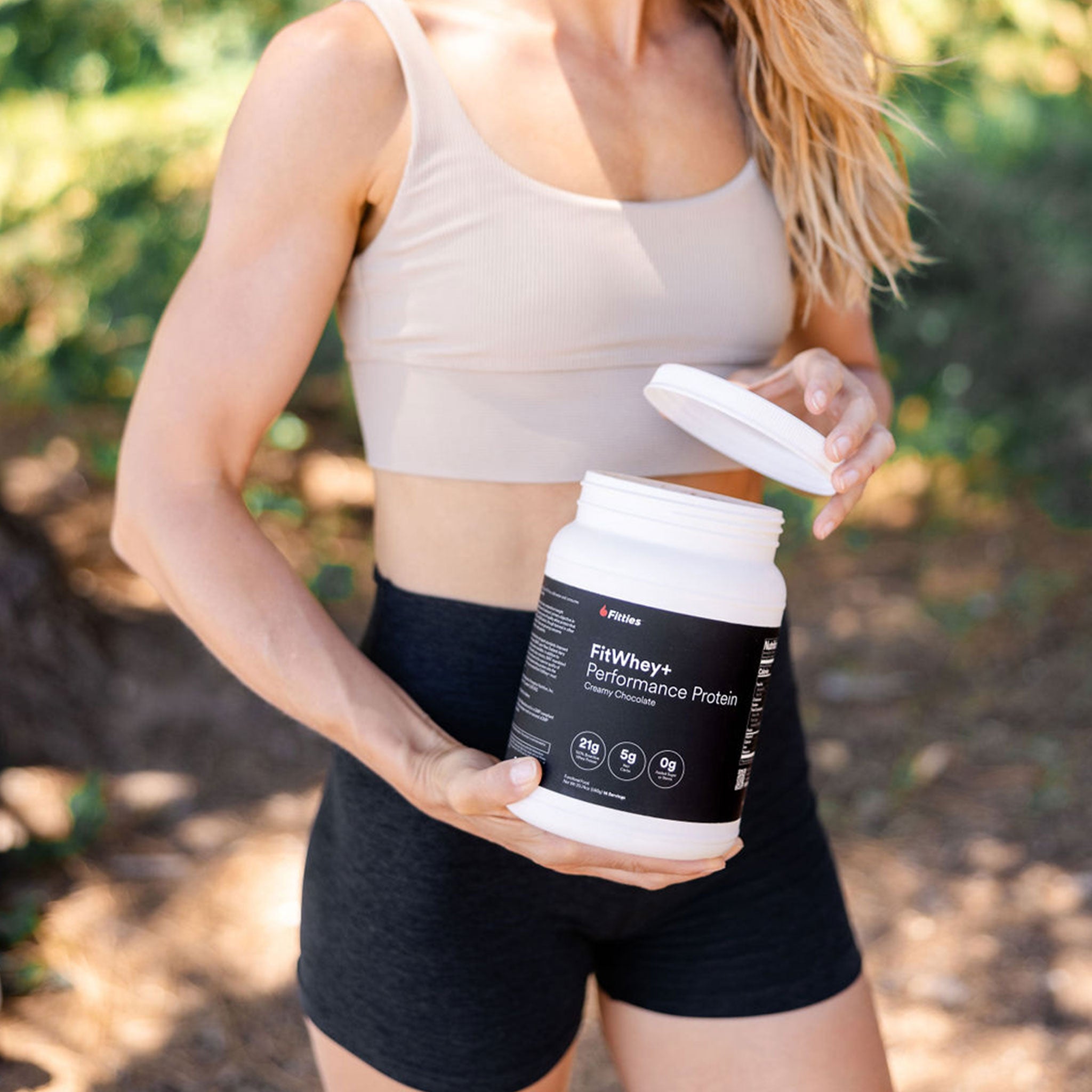 Fit female with a container of FitWhey+ protein powder