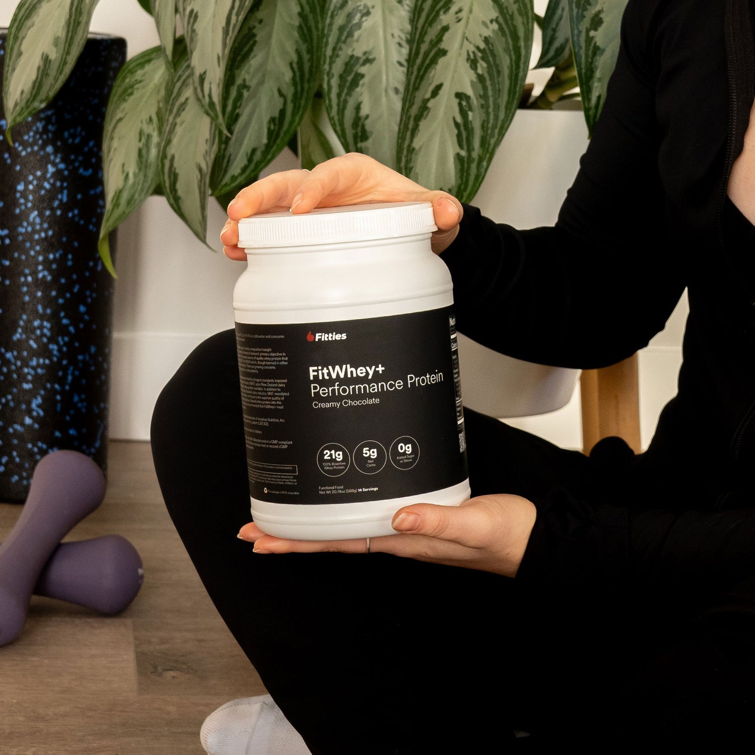 Female yoga instructor holding container of Fitties FitWhey+