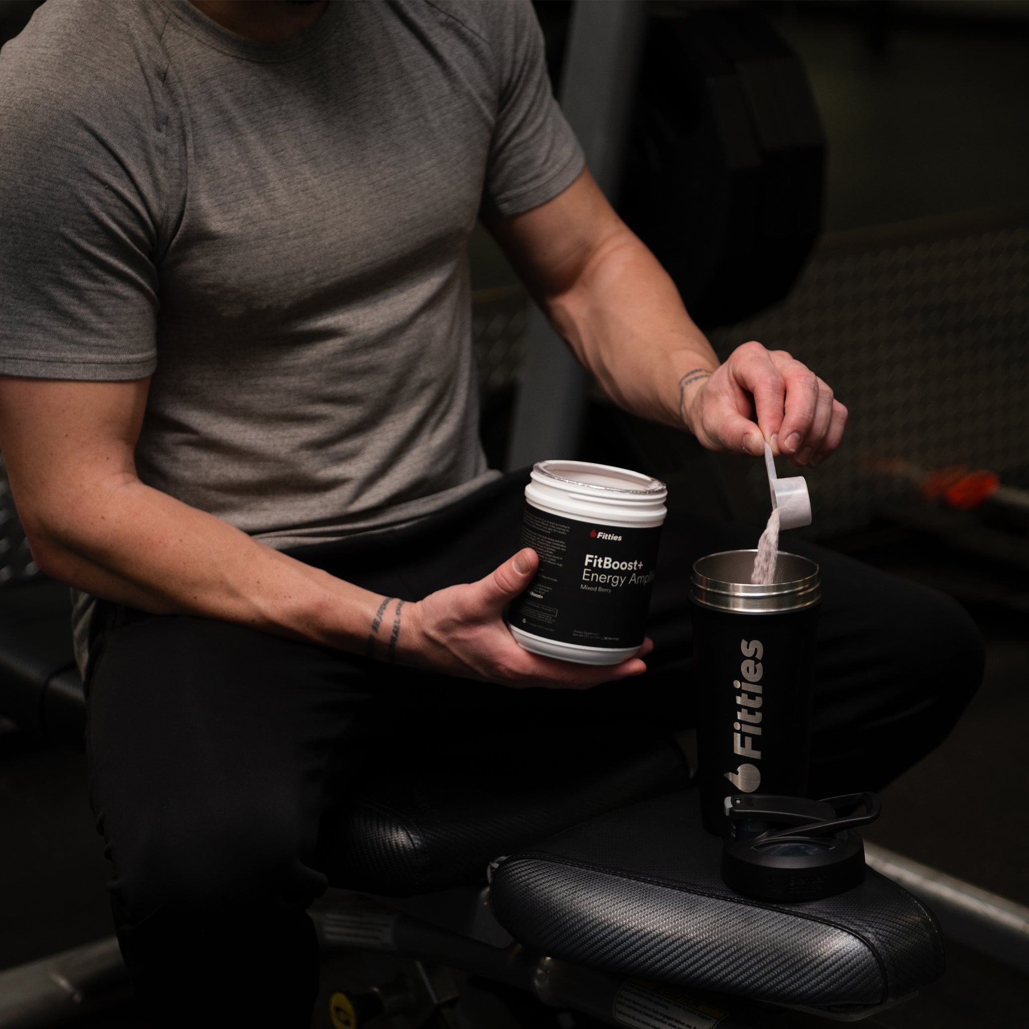 Fit male in gym pouring scoop of FitBoost+ into shaker