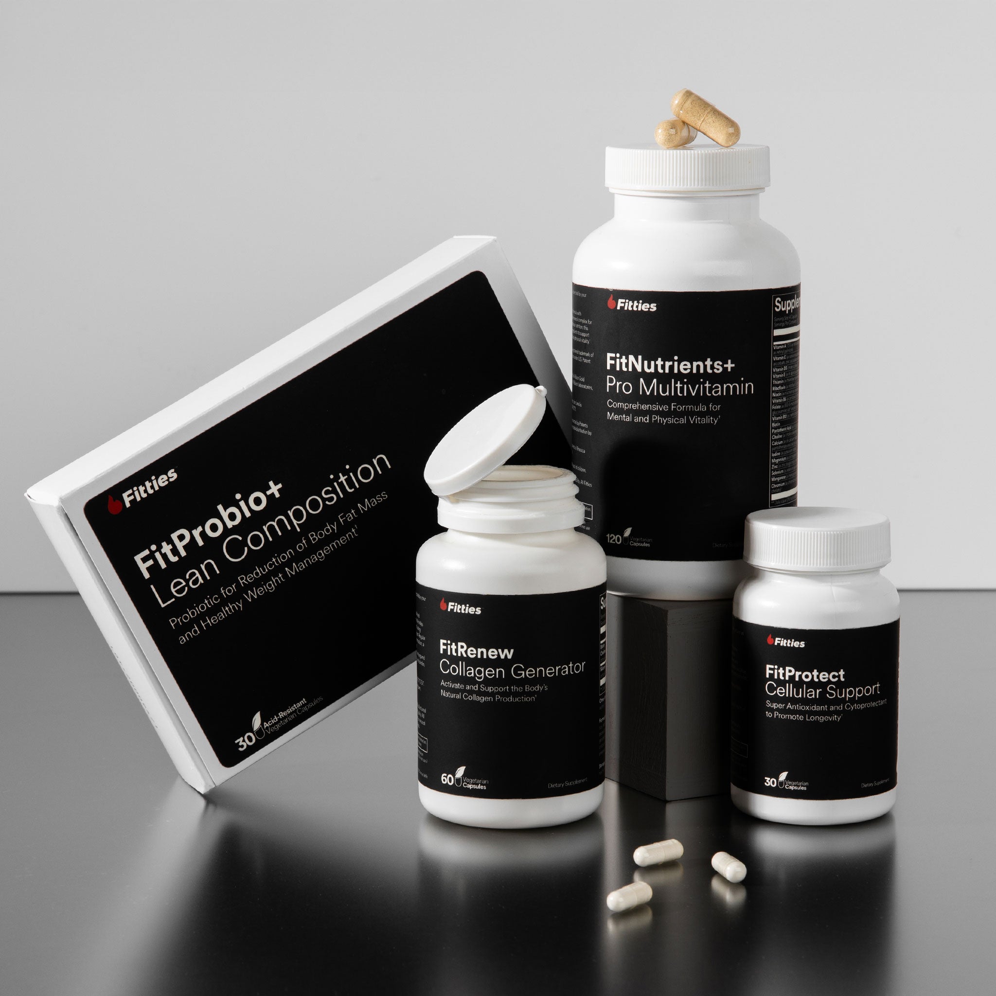 Collection of Fitties supplement bottles and packaging on a reflective surface with a gray background