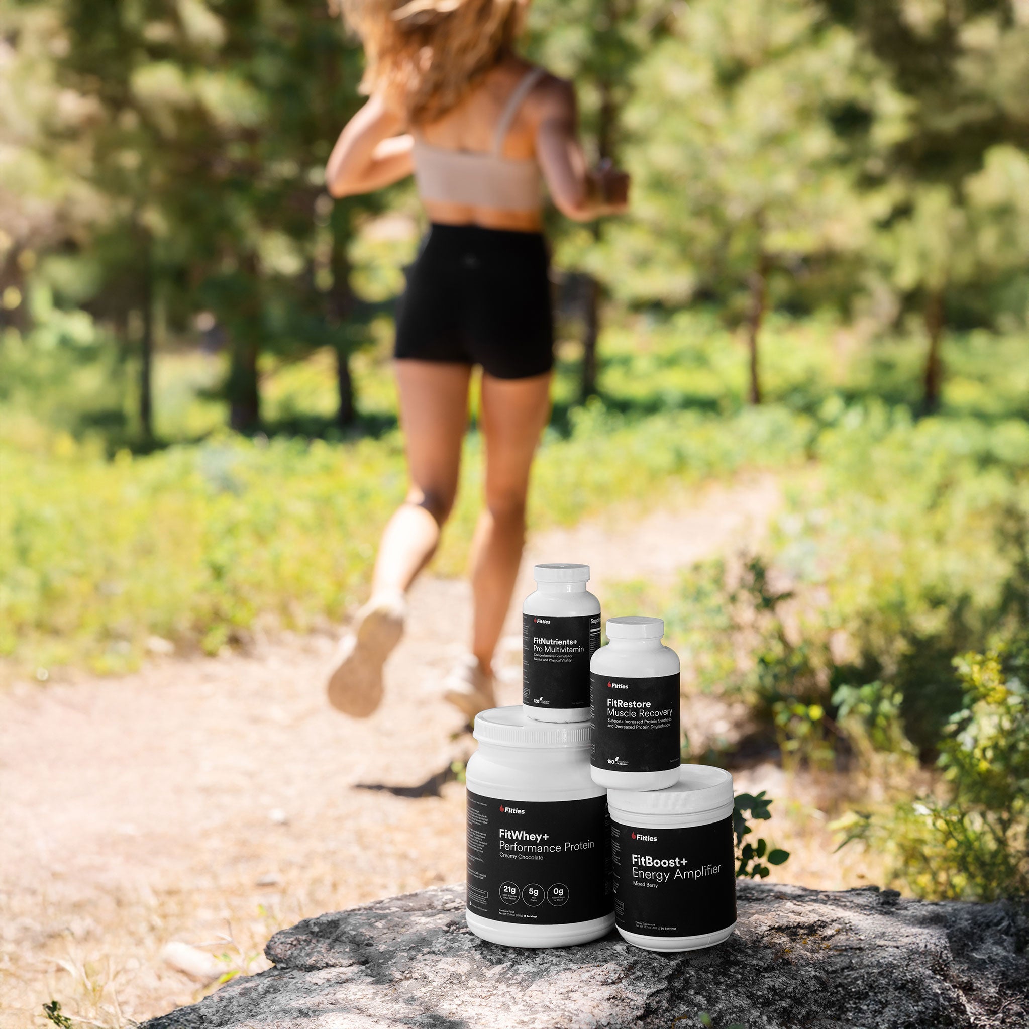 Woman running on a trail with supplement bottles from the Fitties Max Muscle Stack in the foreground