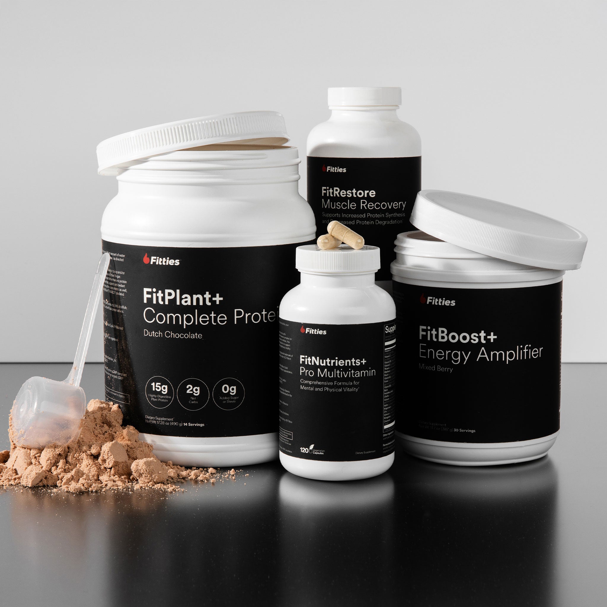 Fitties supplement products, including protein powder, multivitamins, and pre-workout, on a gray surface with a white background.