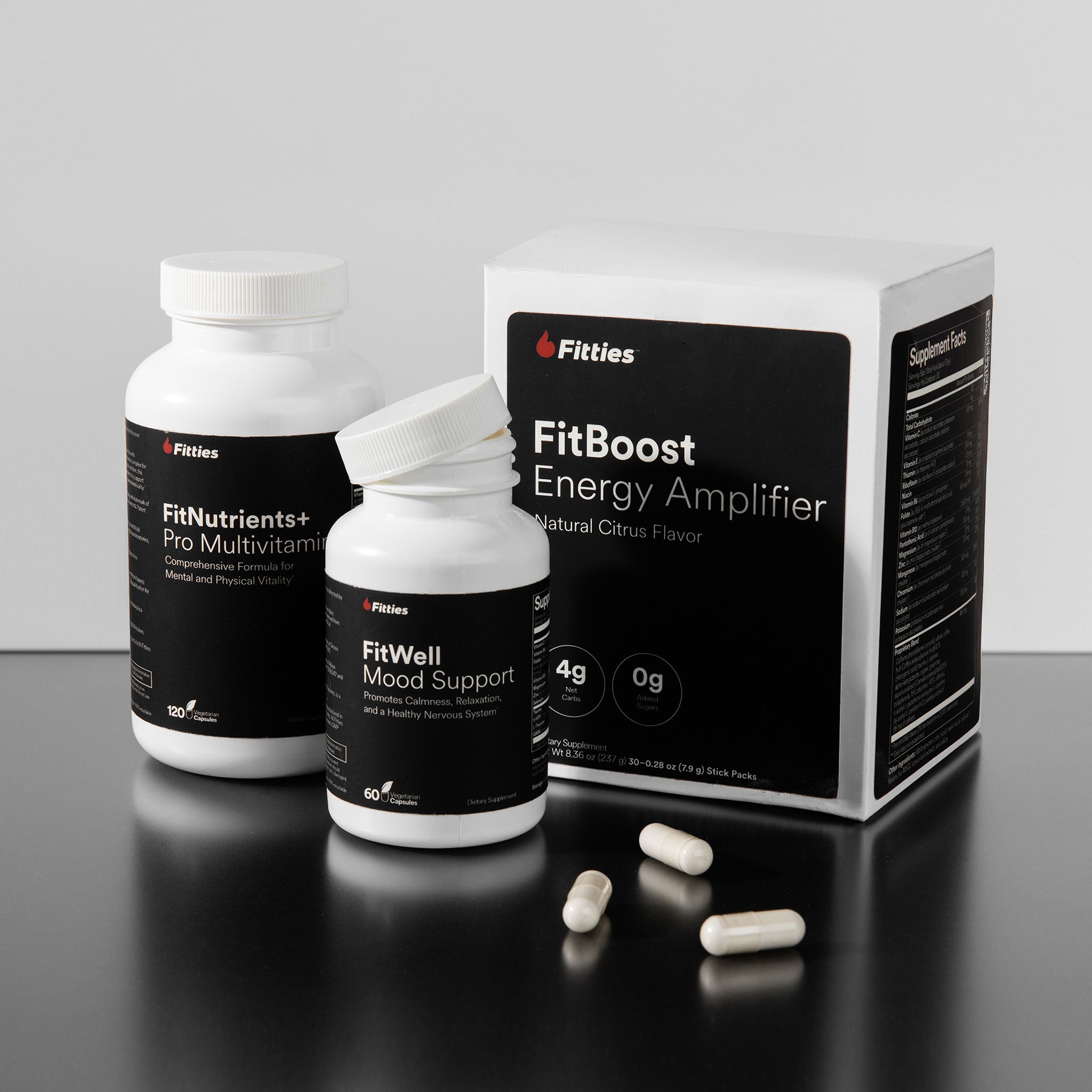 Fitties supplement bottles and packaging on a reflective surface with a gray background