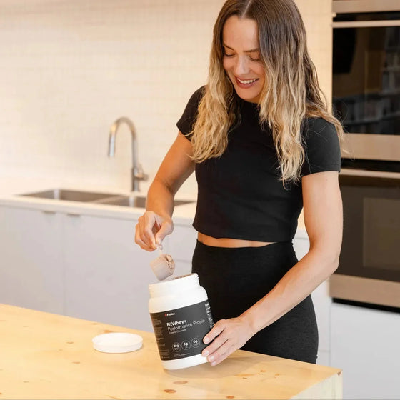 Woman scooping FitWhey+ New Zealand grass-fed whey protein in a kitchen