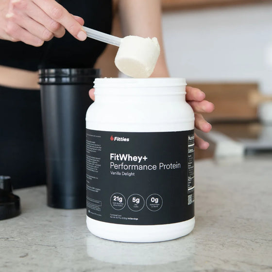 Scooping FitWhey plus vanilla whey protein powder beside a shaker bottle
